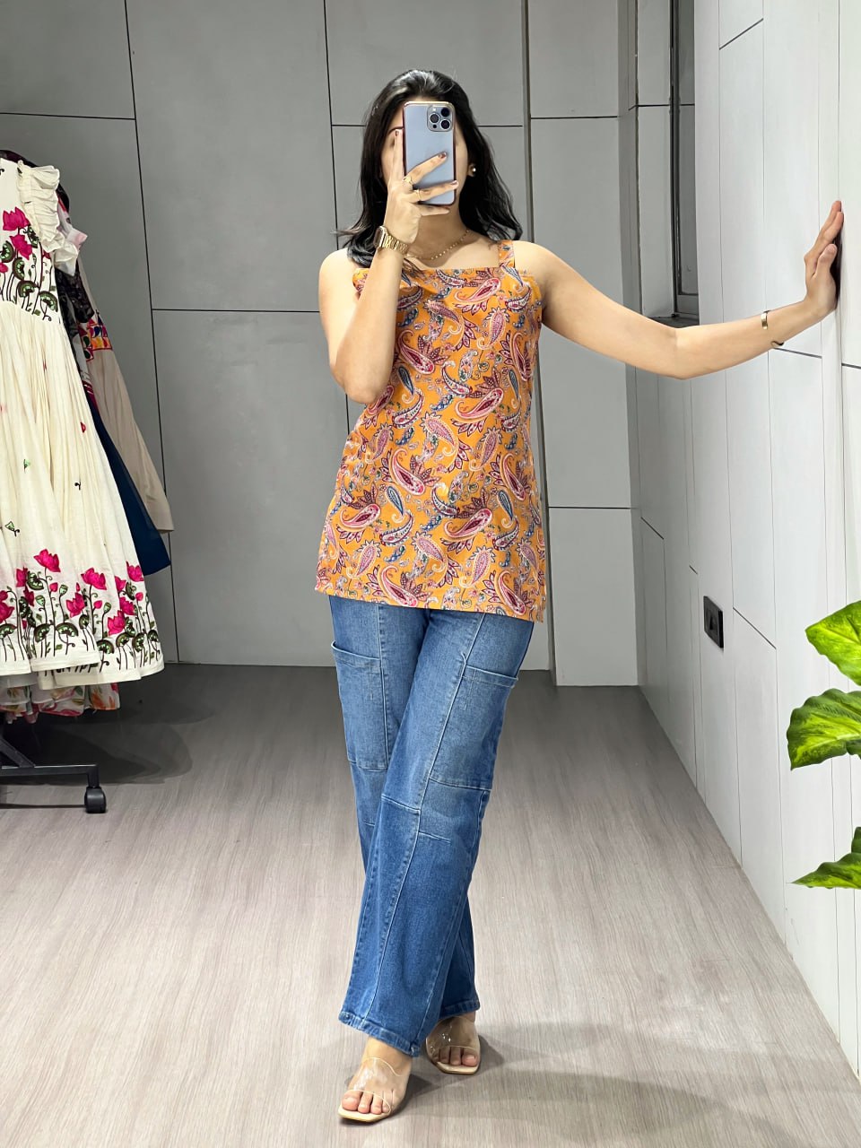 Woman taking a mirror selfie wearing a patterned top and blue jeans in a room.