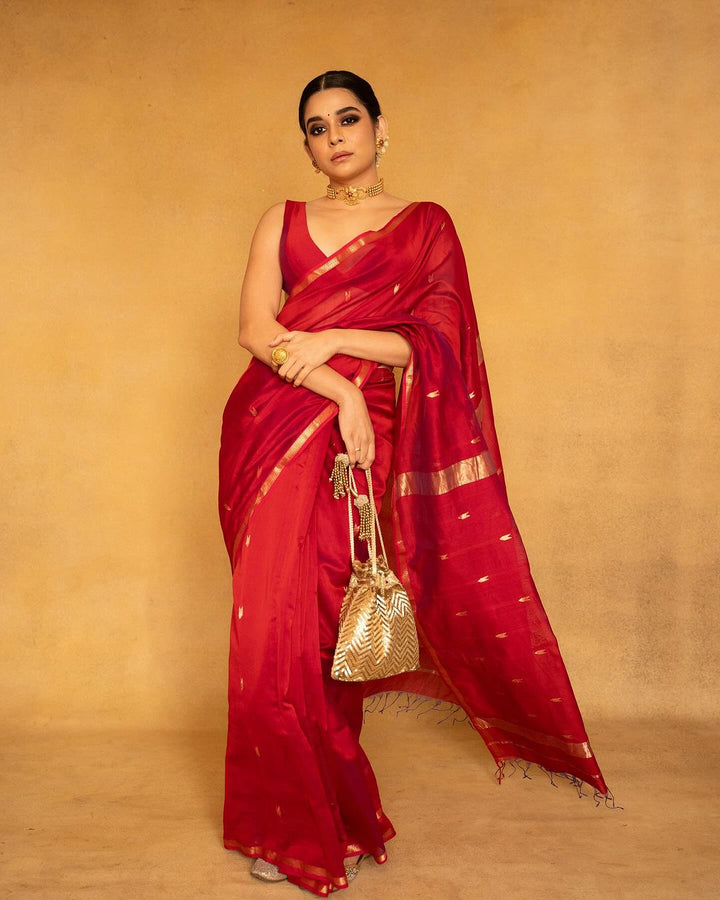 Woman in a red saree with gold accents holding a gold bag against
