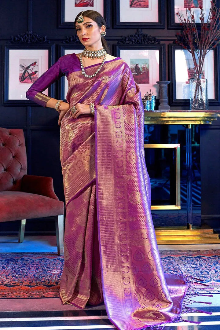 Woman in a traditional saree standing in an elegant room with decor elements.