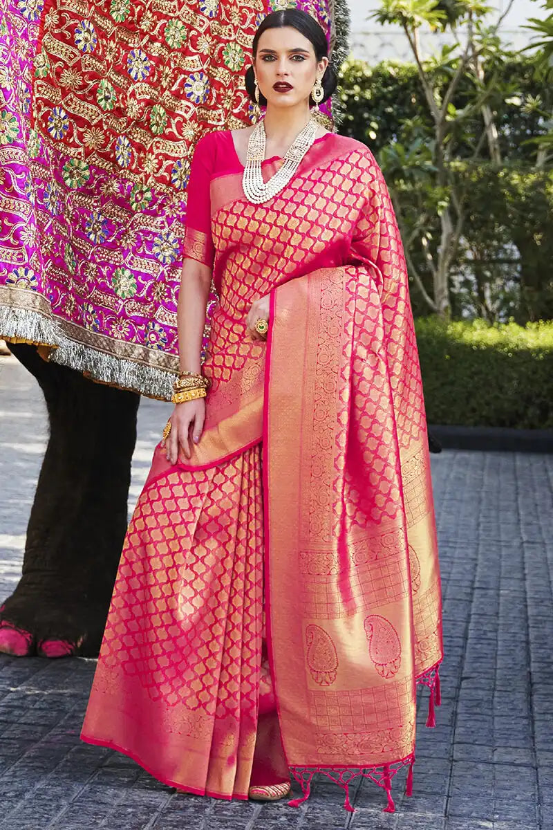 Woman in a pink saree with gold patterns standing outdoors.