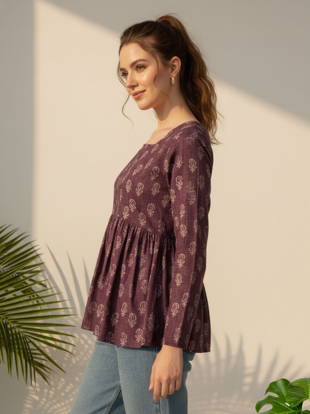 Woman wearing a patterned purple top against a neutral background with plants.