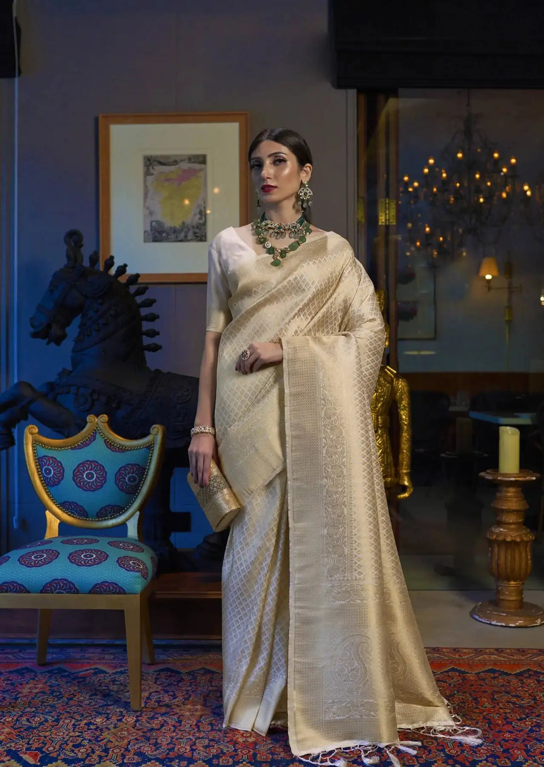 Woman in a cream saree standing in an elegant room with decorative elements.