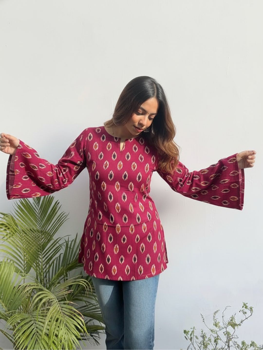 Woman wearing a pink patterned blouse with bell sleeves against a white background