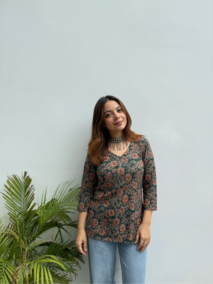 Woman wearing a floral top standing next to a plant against a light blue wall