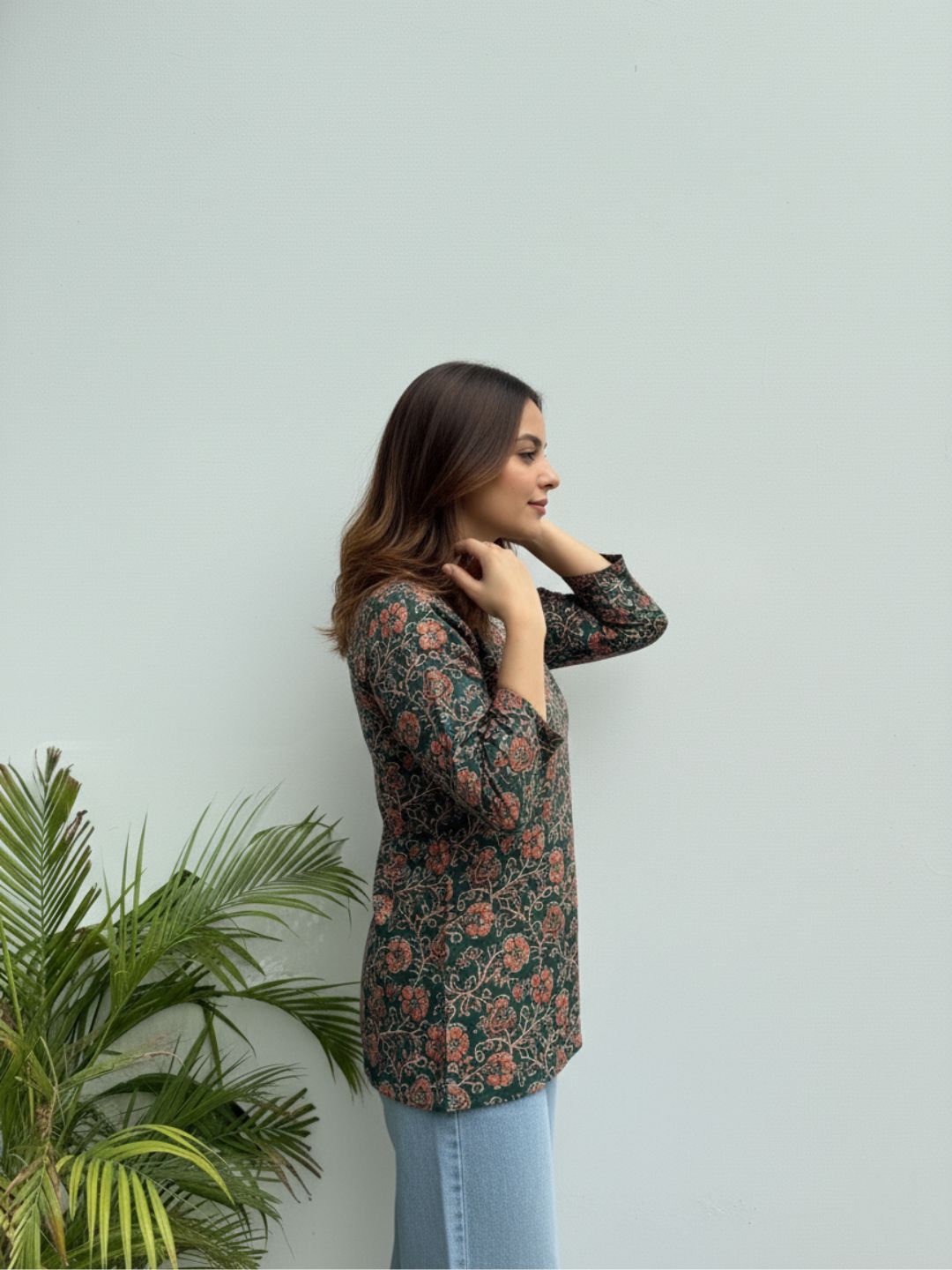 Woman wearing a floral patterned shirt against a light gray background with a plant to the left.