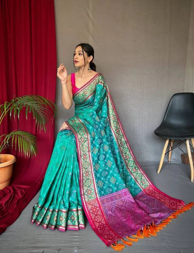 Woman wearing a teal saree with pink blouse against a gray wall.
