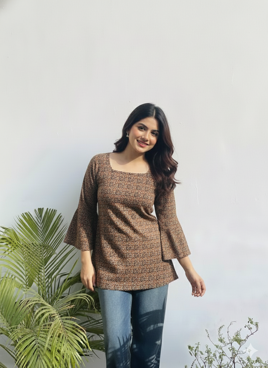 Woman wearing a brown top and blue jeans standing in front of a white wall with green plants.