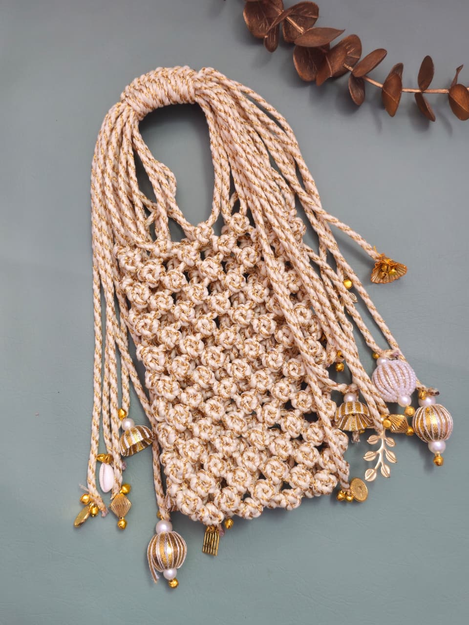Beige crocheted bag with decorative tassels on a gray background
