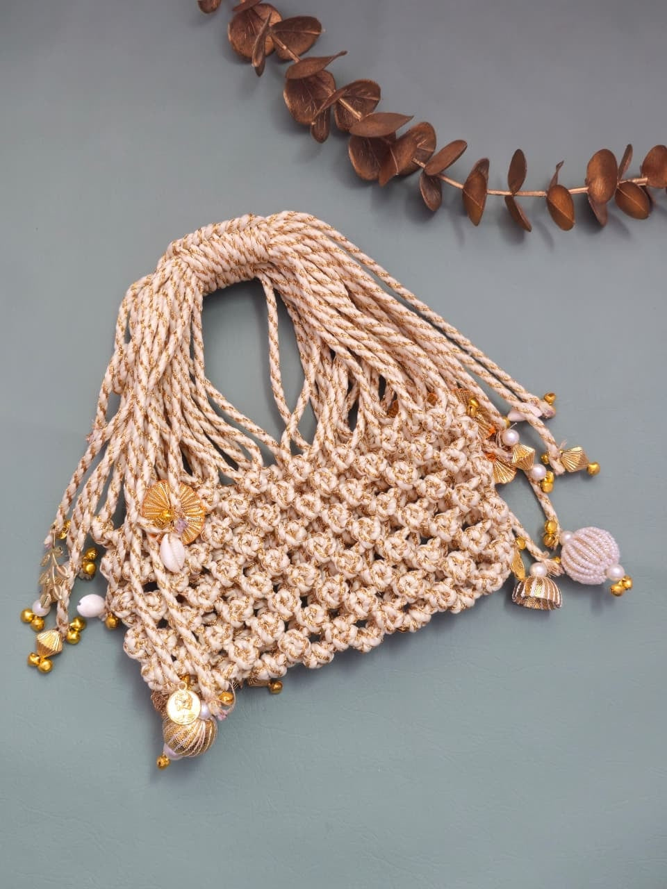 Beige woven bag with tassels and beads on a gray background