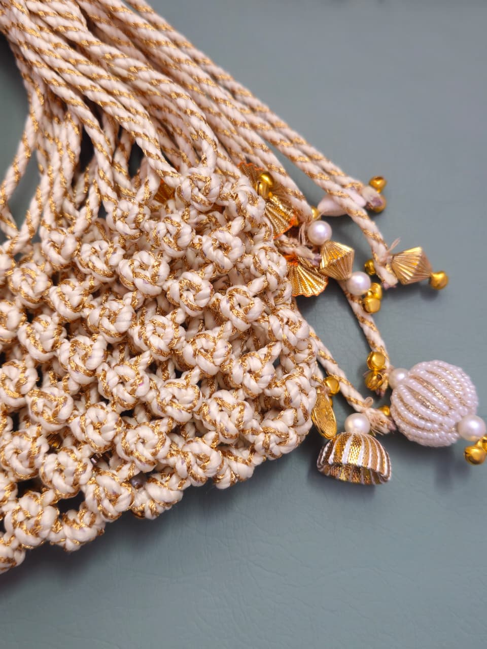 Beige knitted rope with gold and pearl embellishments on a gray background