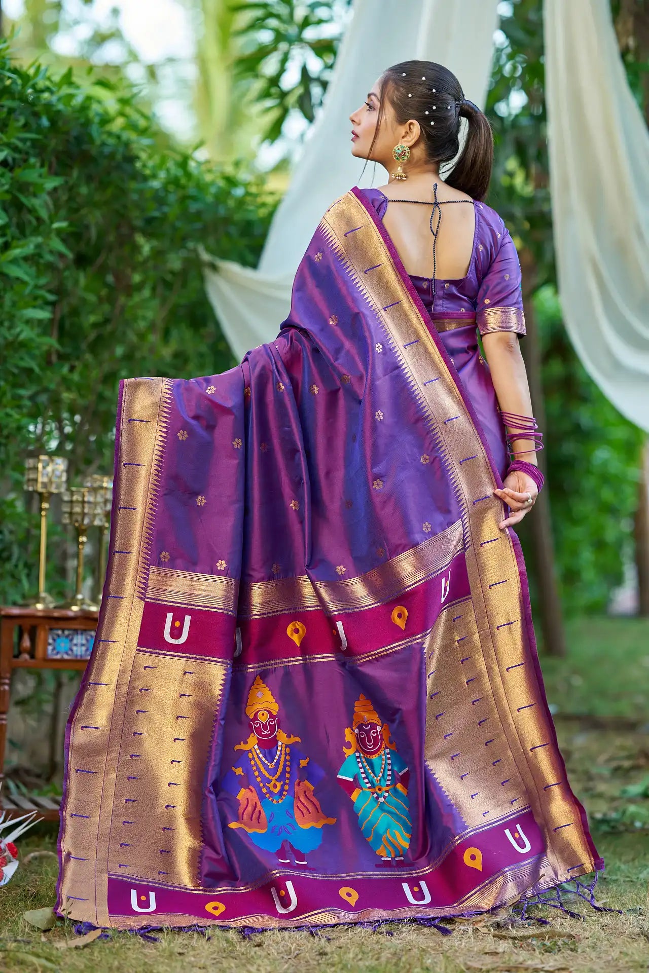 Woman wearing a traditional purple saree with gold patterns outdoors.