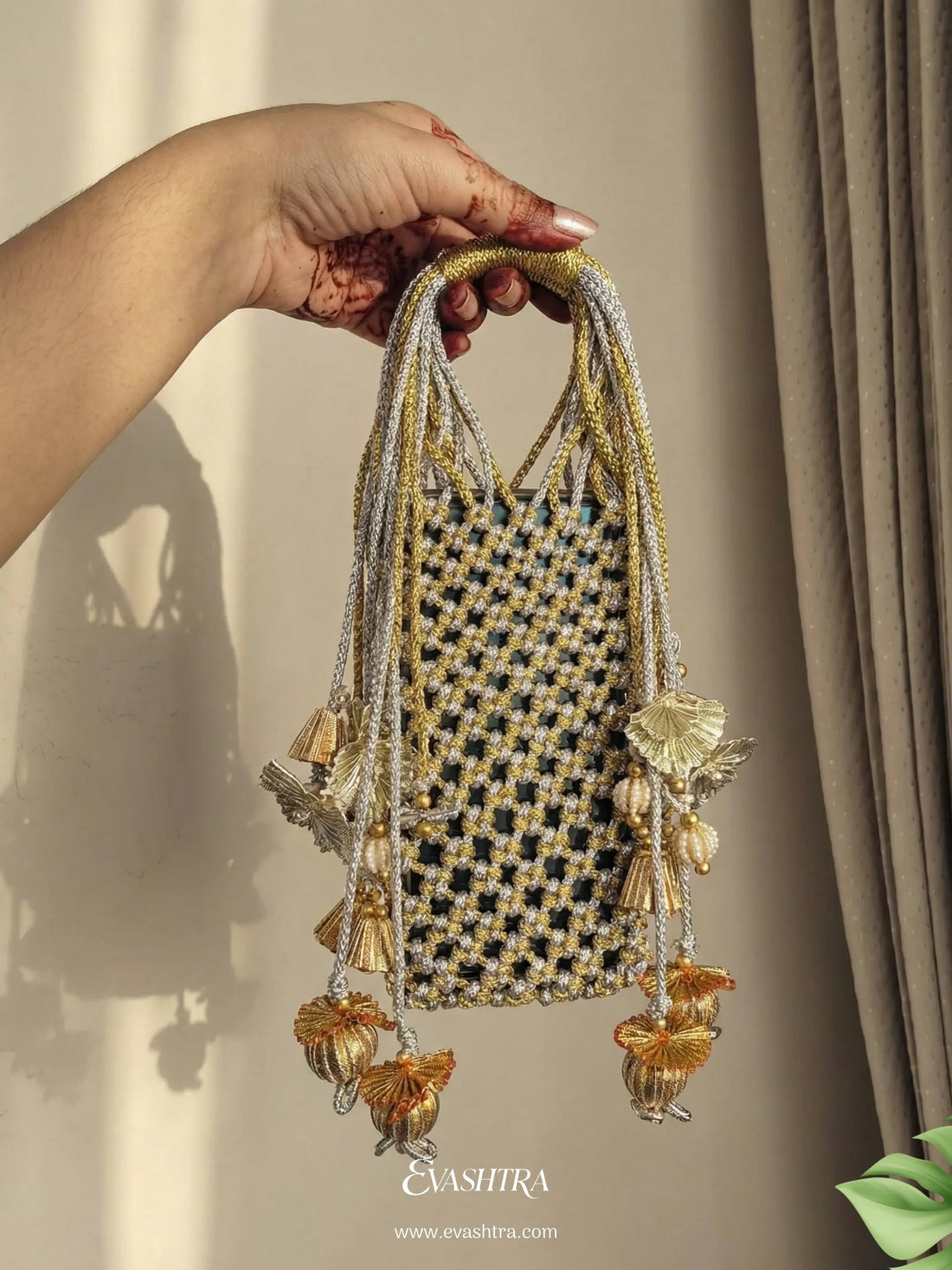Hand holding a decorative bag with tassels against a neutral background