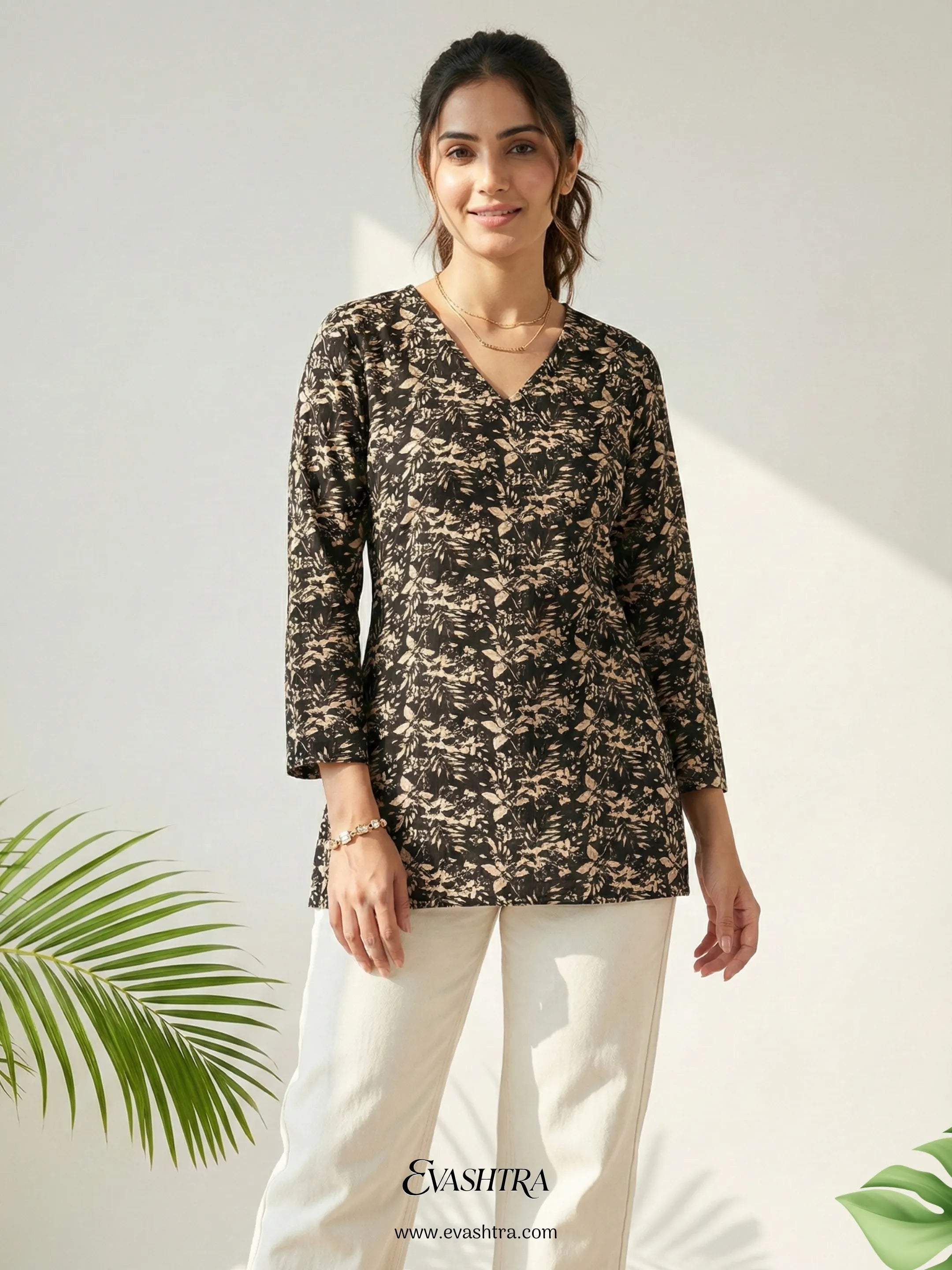 Woman wearing a patterned top and white pants with a green leafy background