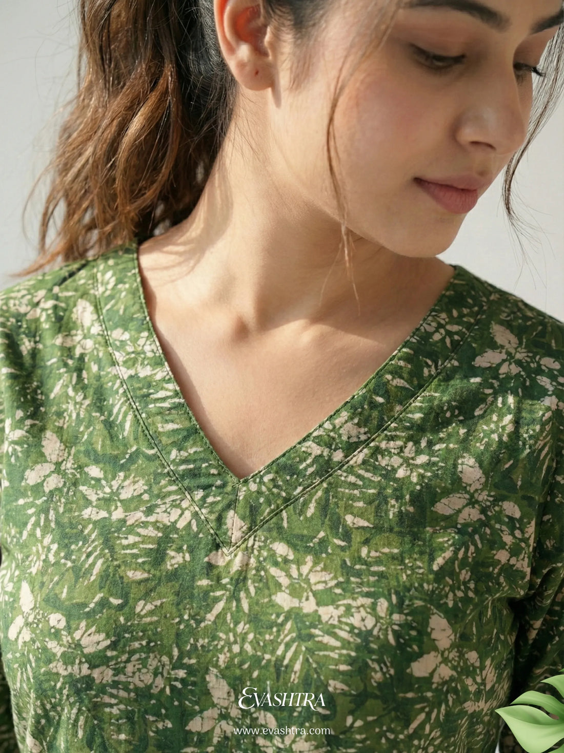 Woman wearing a green floral blouse with 'EvaShri' branding.