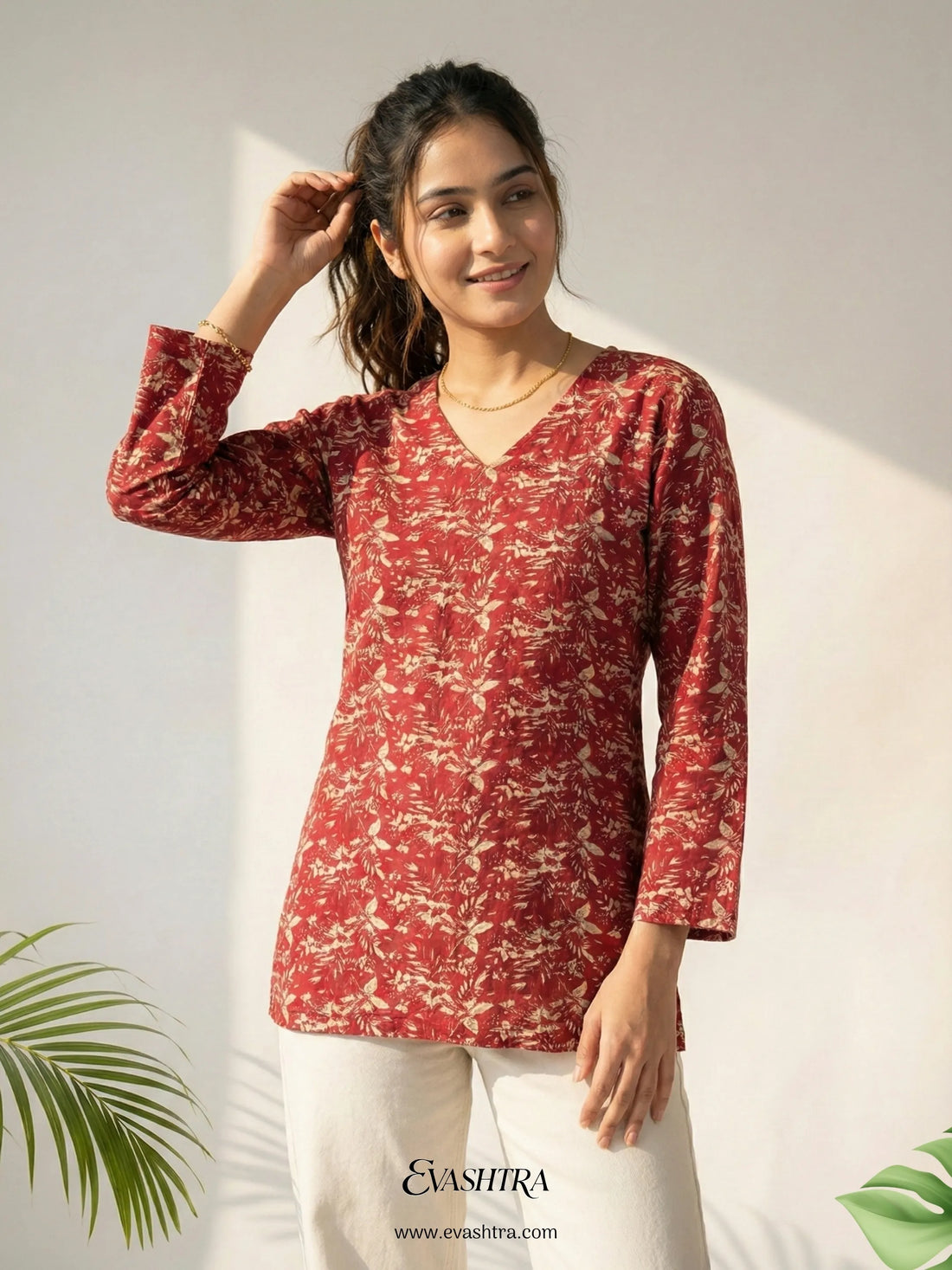 Woman wearing a red patterned top with white pants against a light background