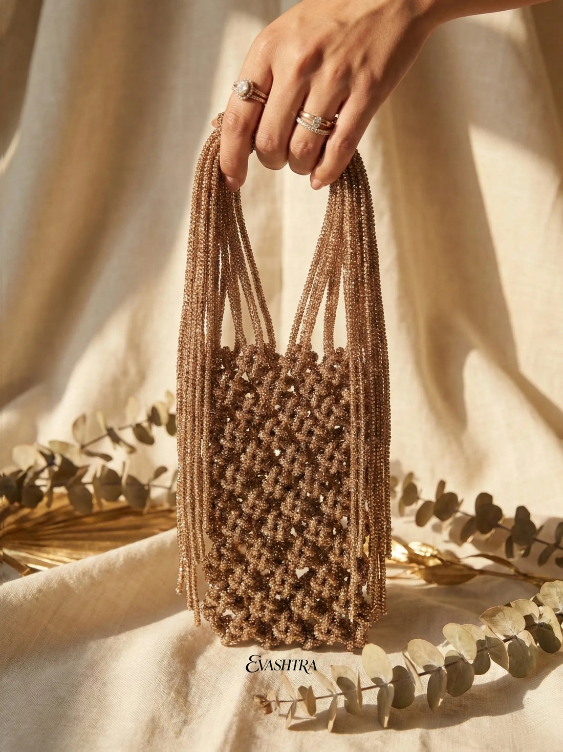 Hand holding a woven brown bag with 'Eashtra' branding on a neutral background.