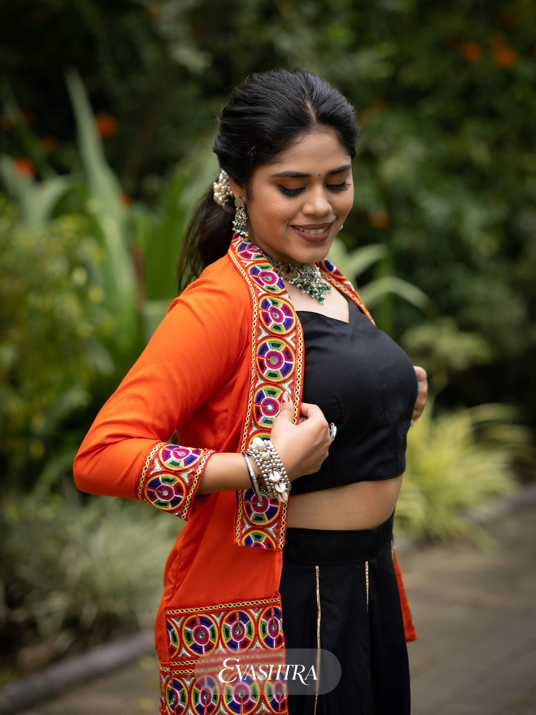 Woman in traditional attire with a colorful blouse and black saree, standing outdoors.