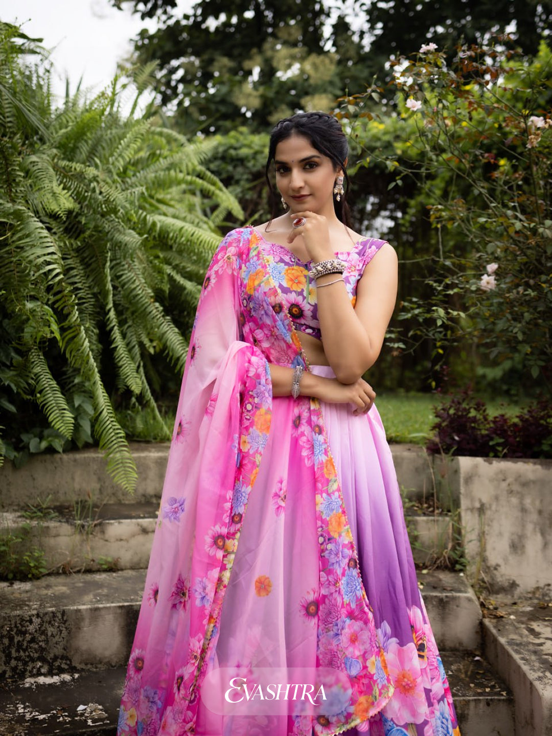 Woman in a colorful floral dress standing outdoors with greenery in the background