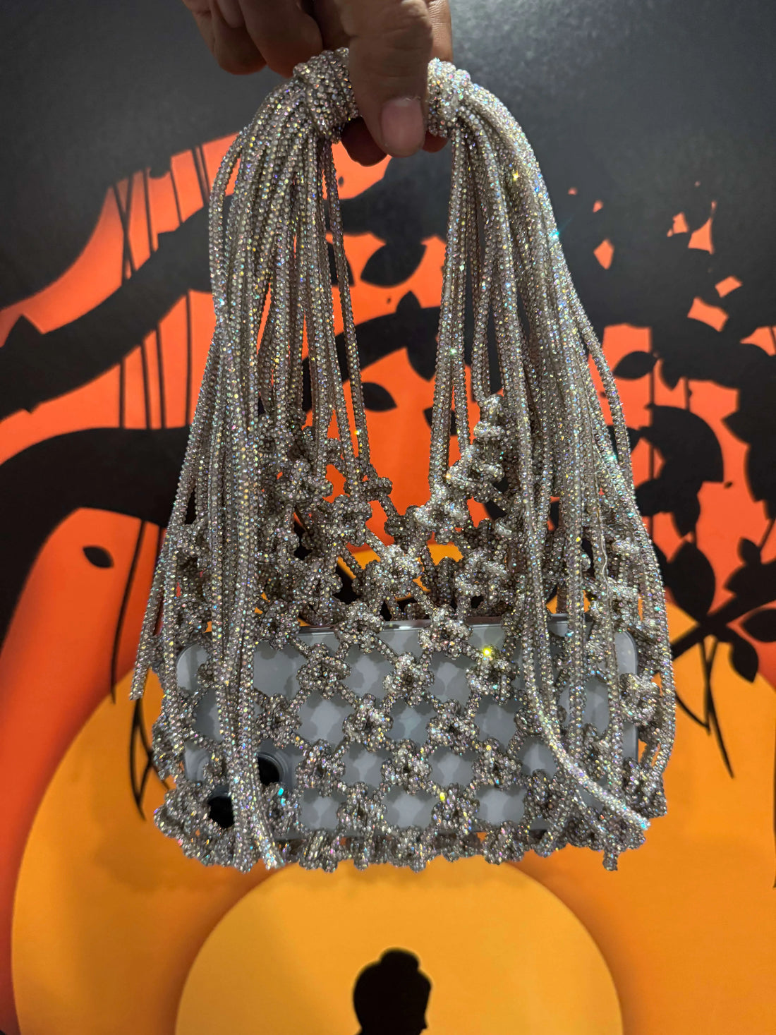 Silver beaded bag held by a hand against an orange and black abstract background