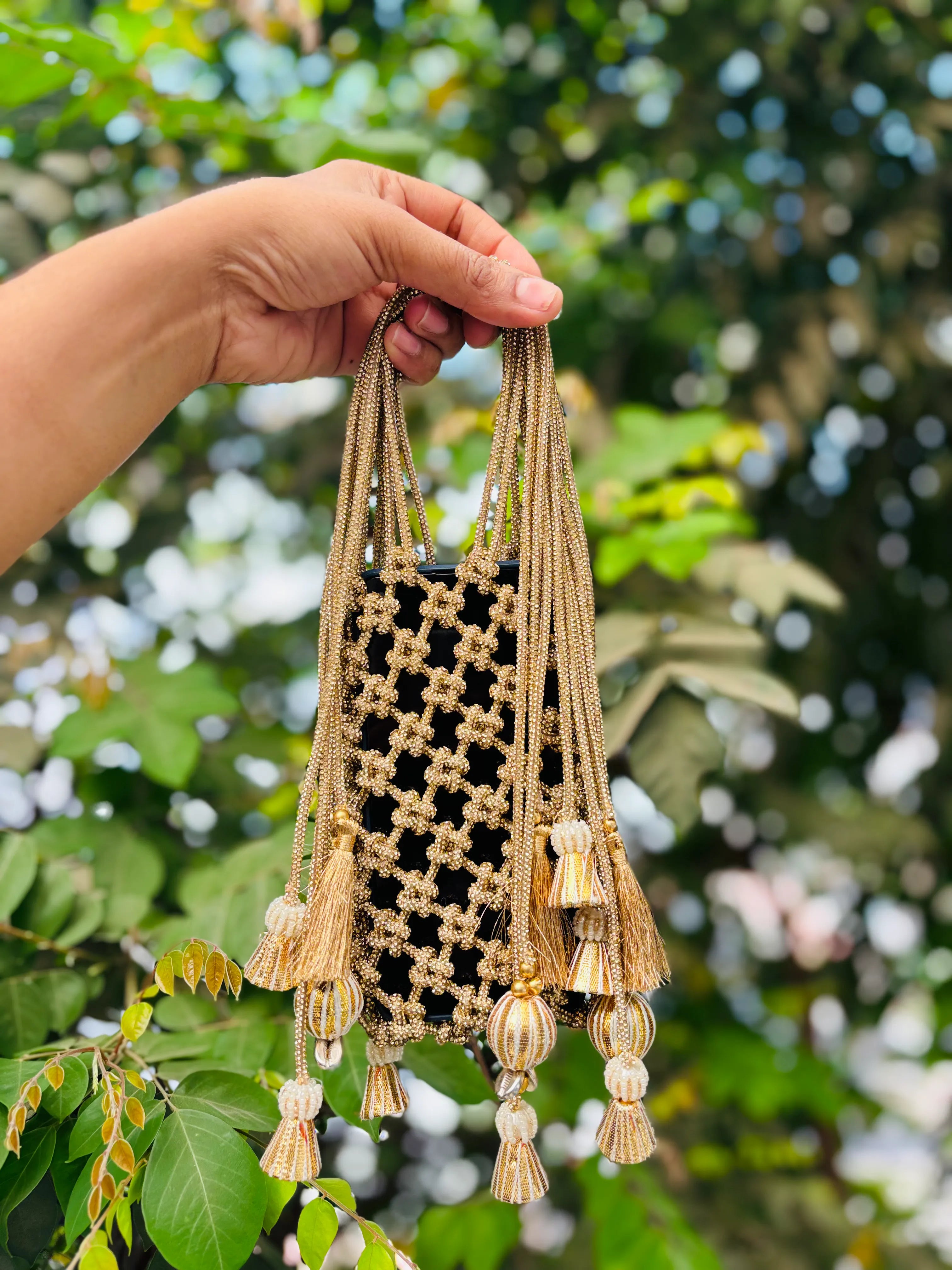 Hand holding a decorative bag with tassels against a blurred green leafy background