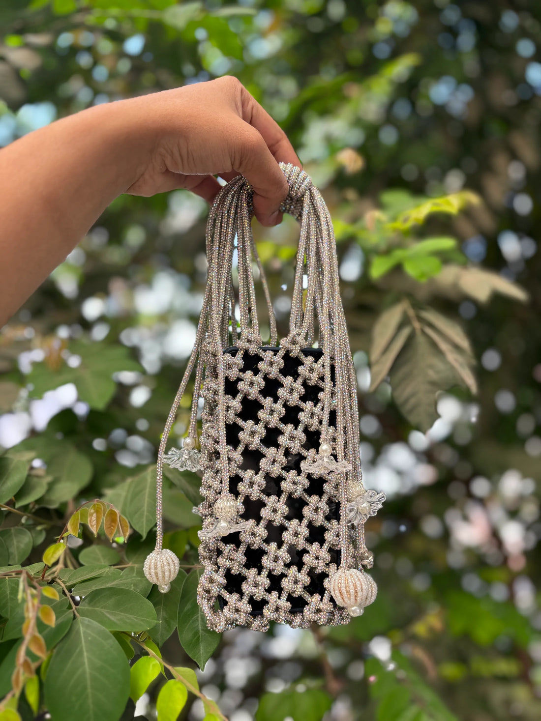 Hand holding a woven bag with a blurred green leafy background