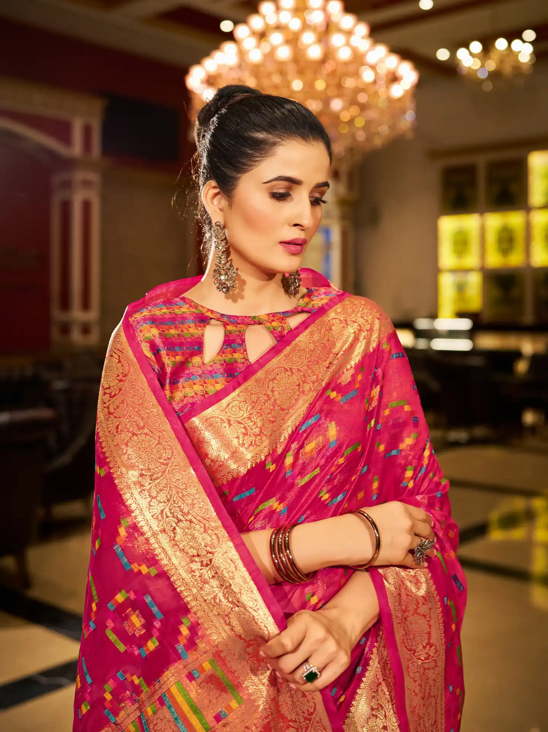 Woman wearing a vibrant pink saree with gold patterns in an indoor setting.