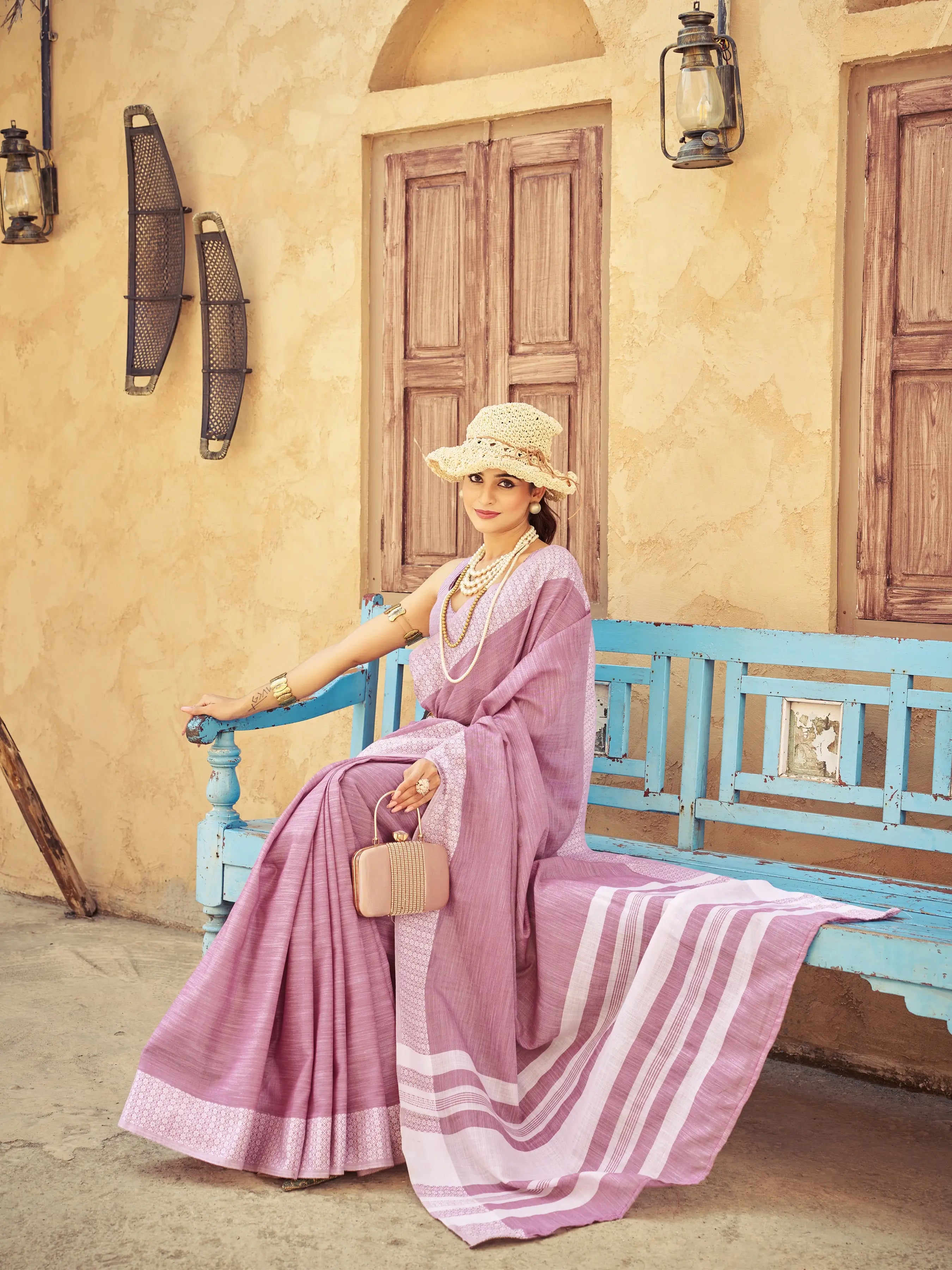 Woman in a pink saree sitting on a blue bench in a rustic setting.