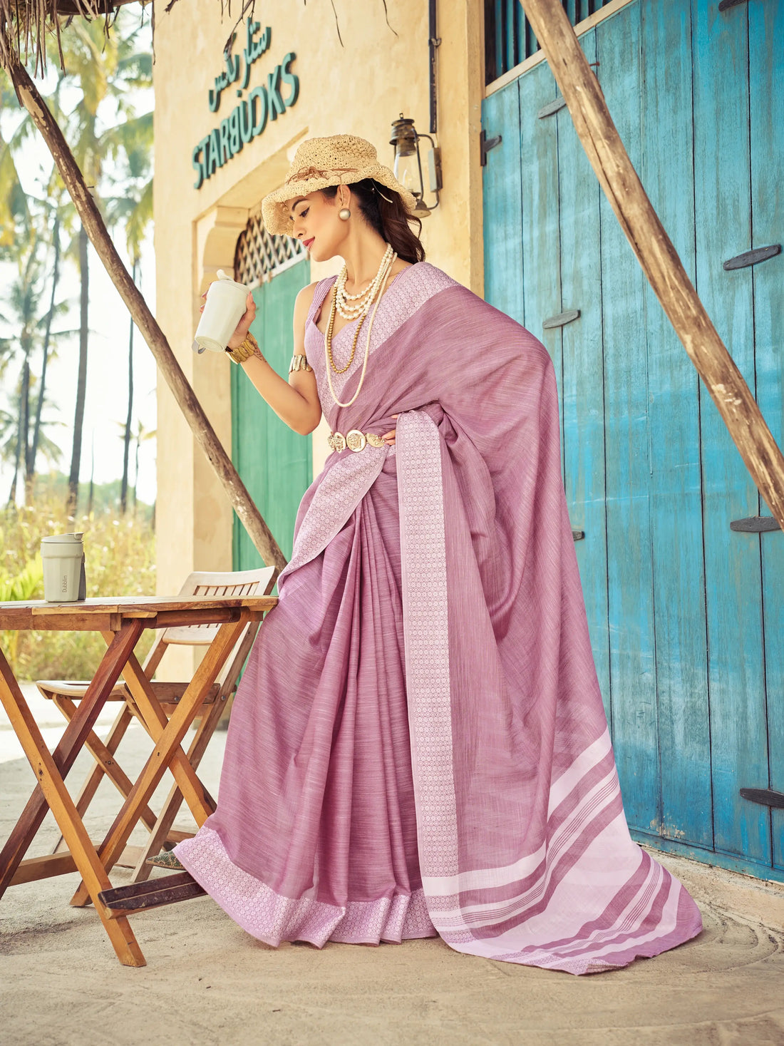 Woman in a pink saree standing in front of a blue door with 'Harbours' sign.
