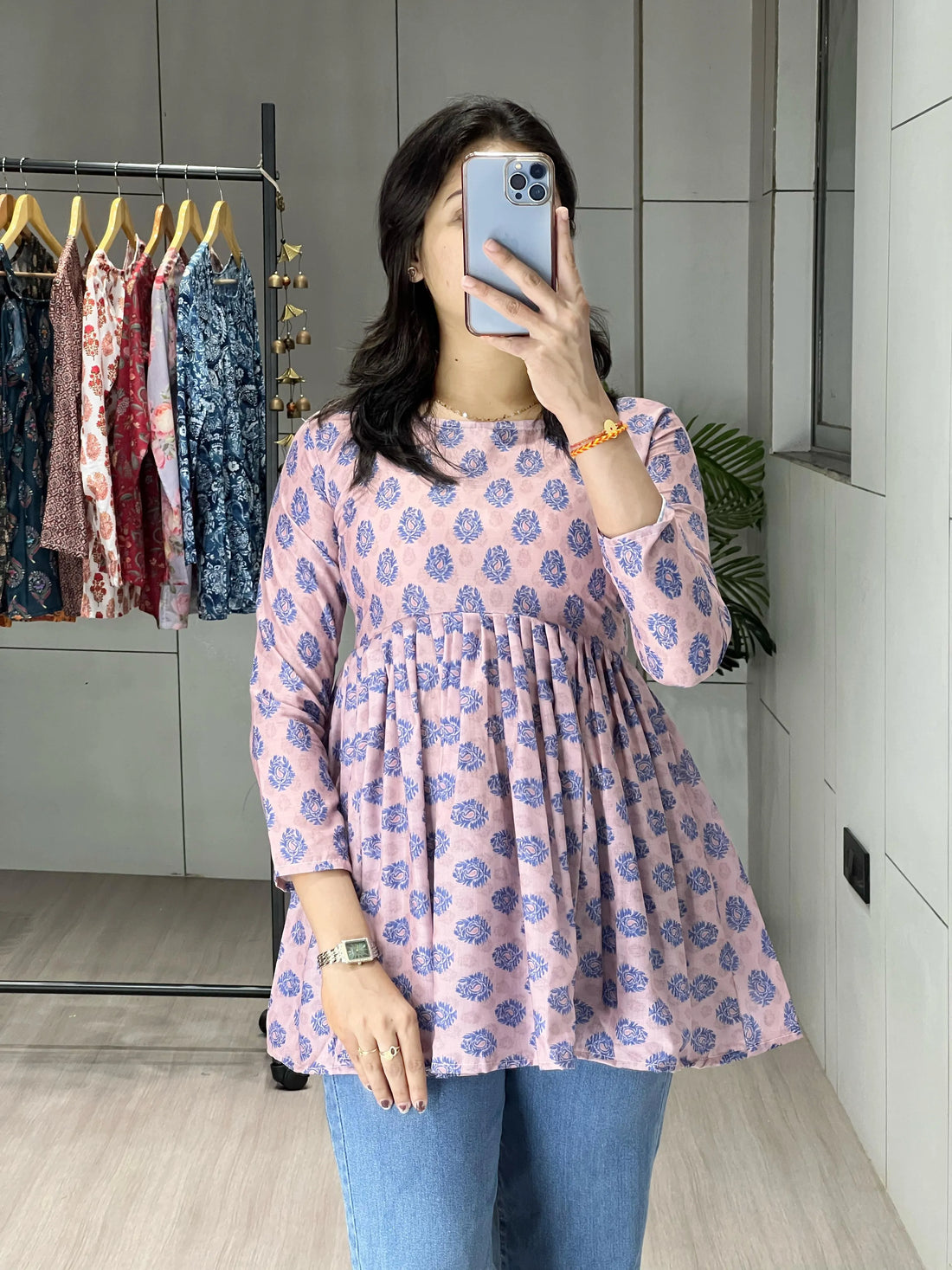 Woman taking a mirror selfie wearing a pink floral dress in a clothing store.