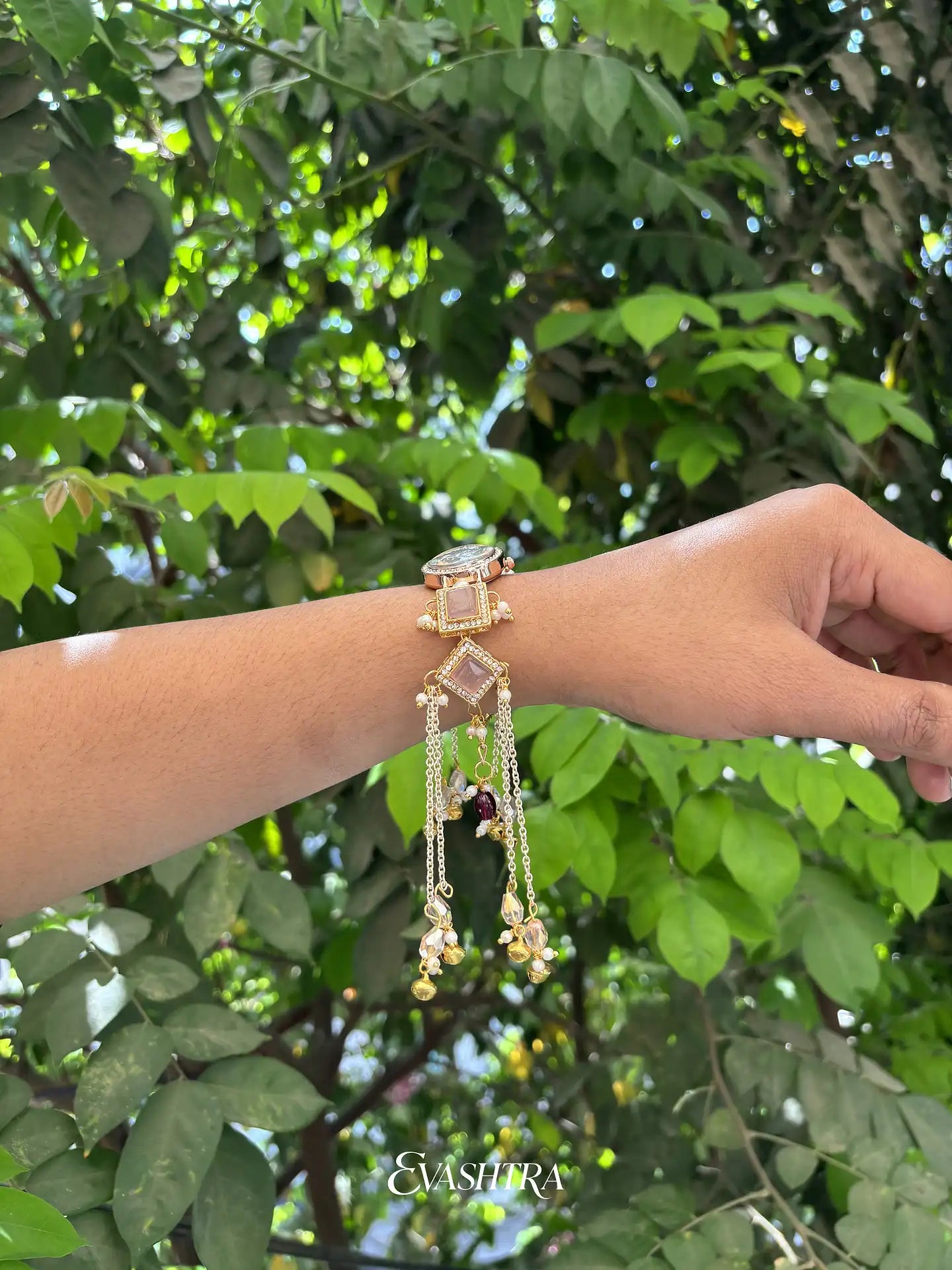 Hand wearing a decorative bracelet with green foliage in the background