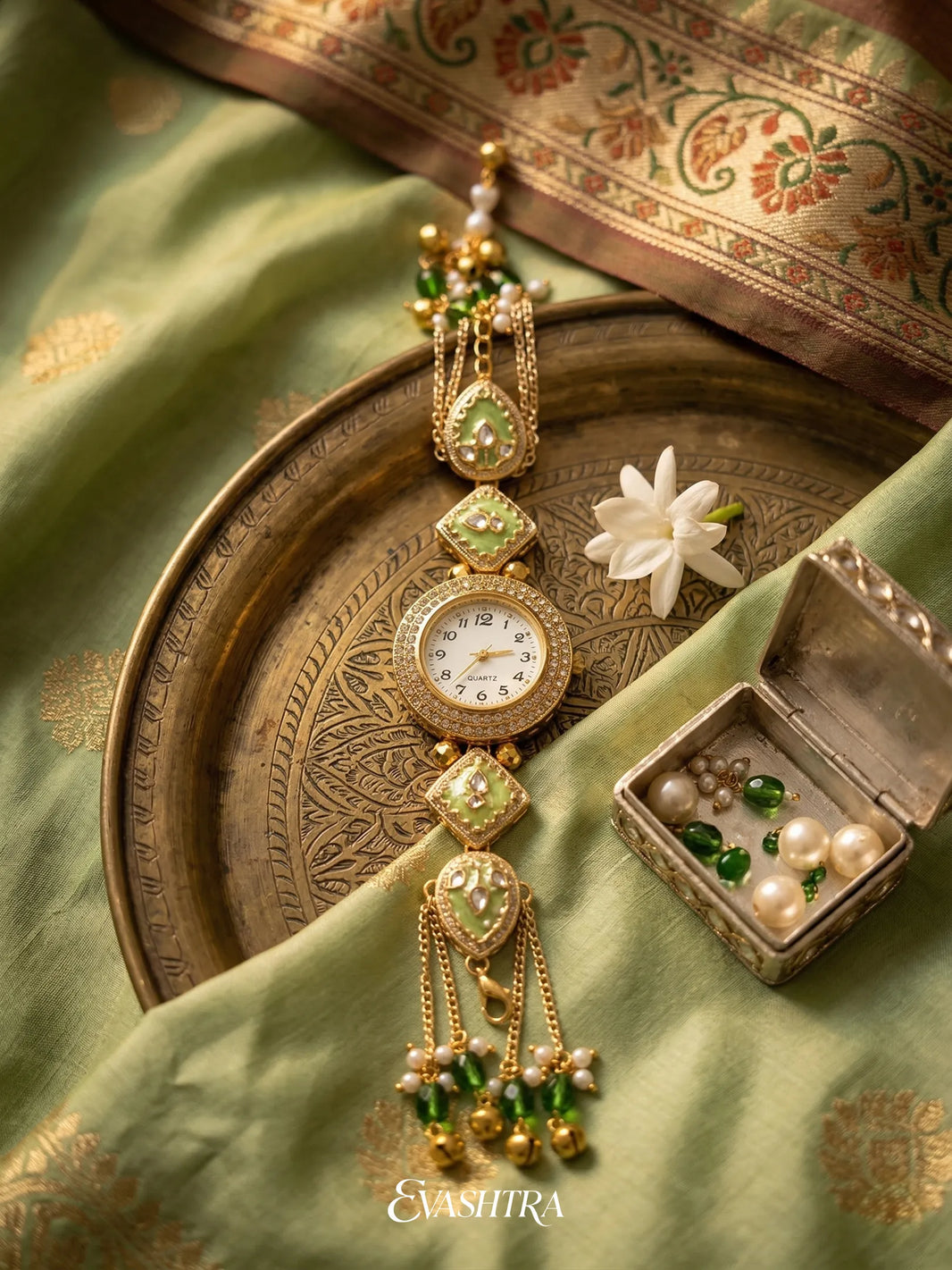 Decorative gold and green jewelry set on a green fabric background with 'Evastra' branding.