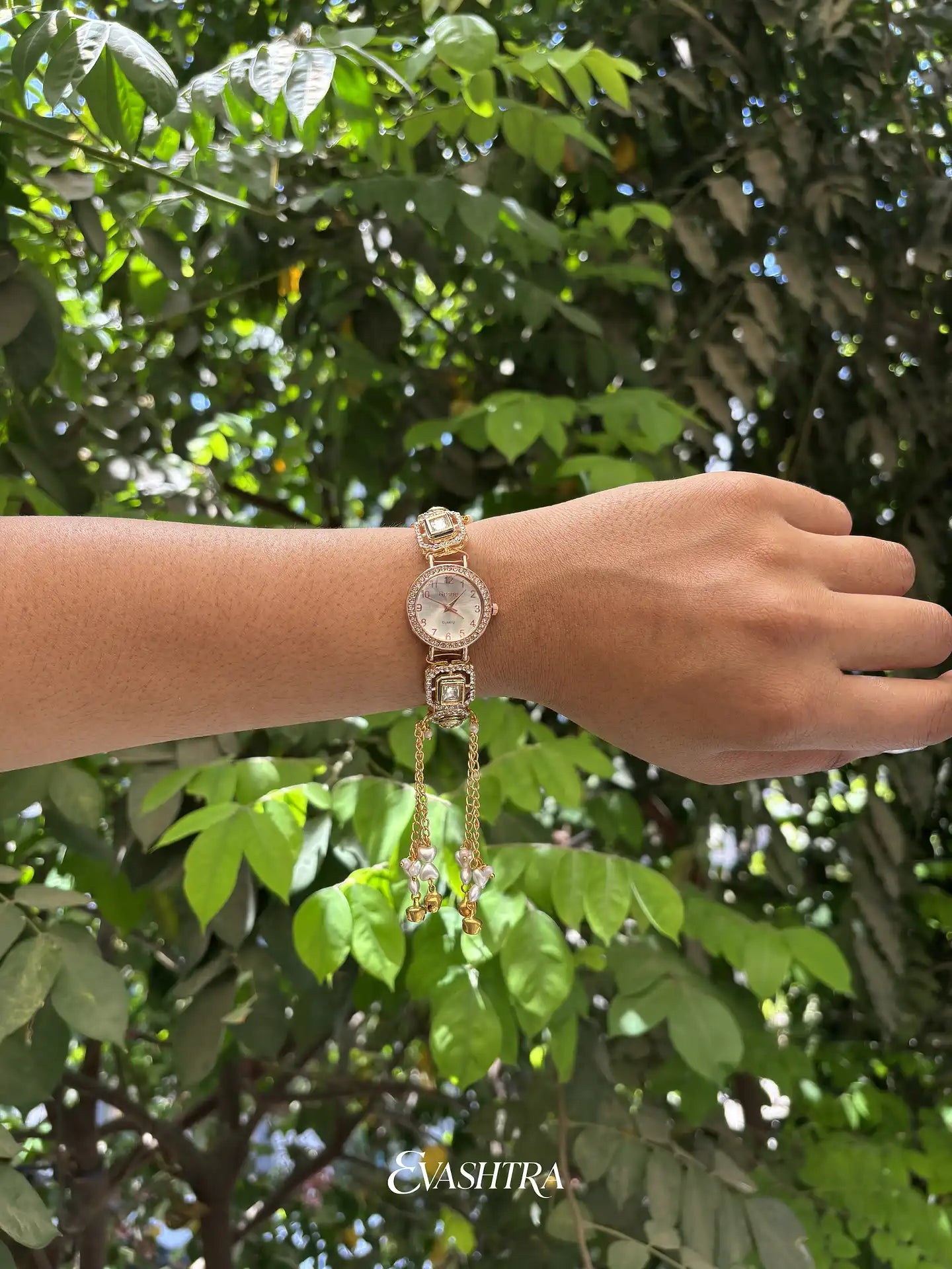 Hand wearing a watch with a green leafy background