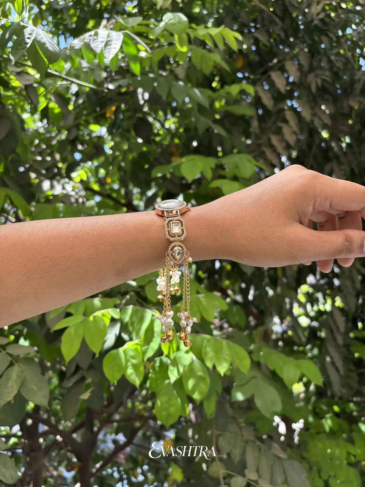 Hand wearing a decorative bracelet with a blurred green leafy background