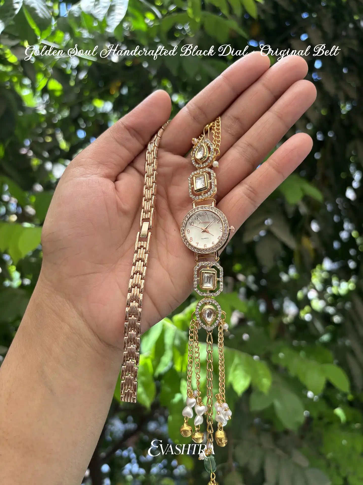 Hand holding a gold watch with decorative chain against a green leafy background