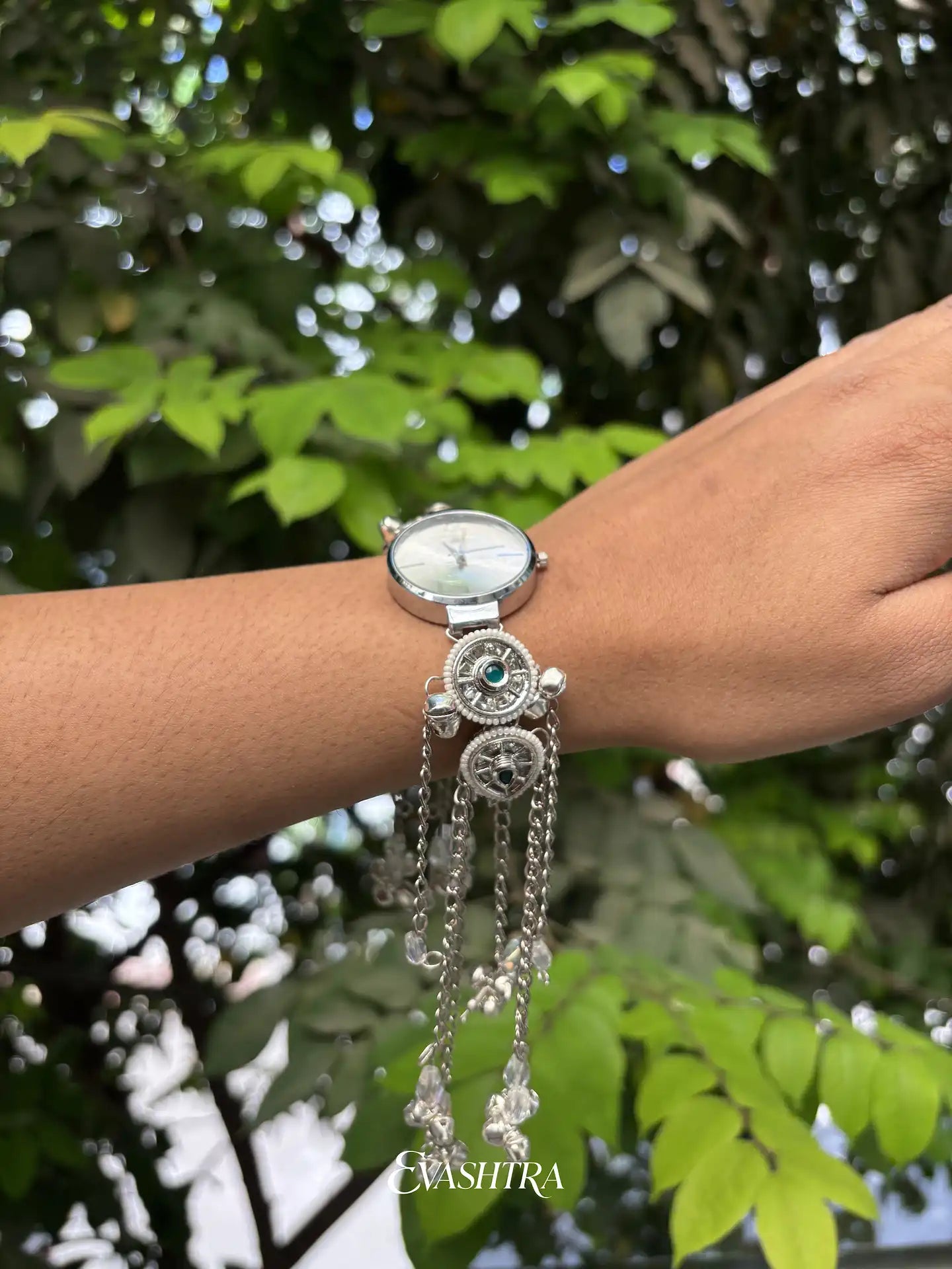 Silver watch with dangling chain on a wrist against a green leafy background