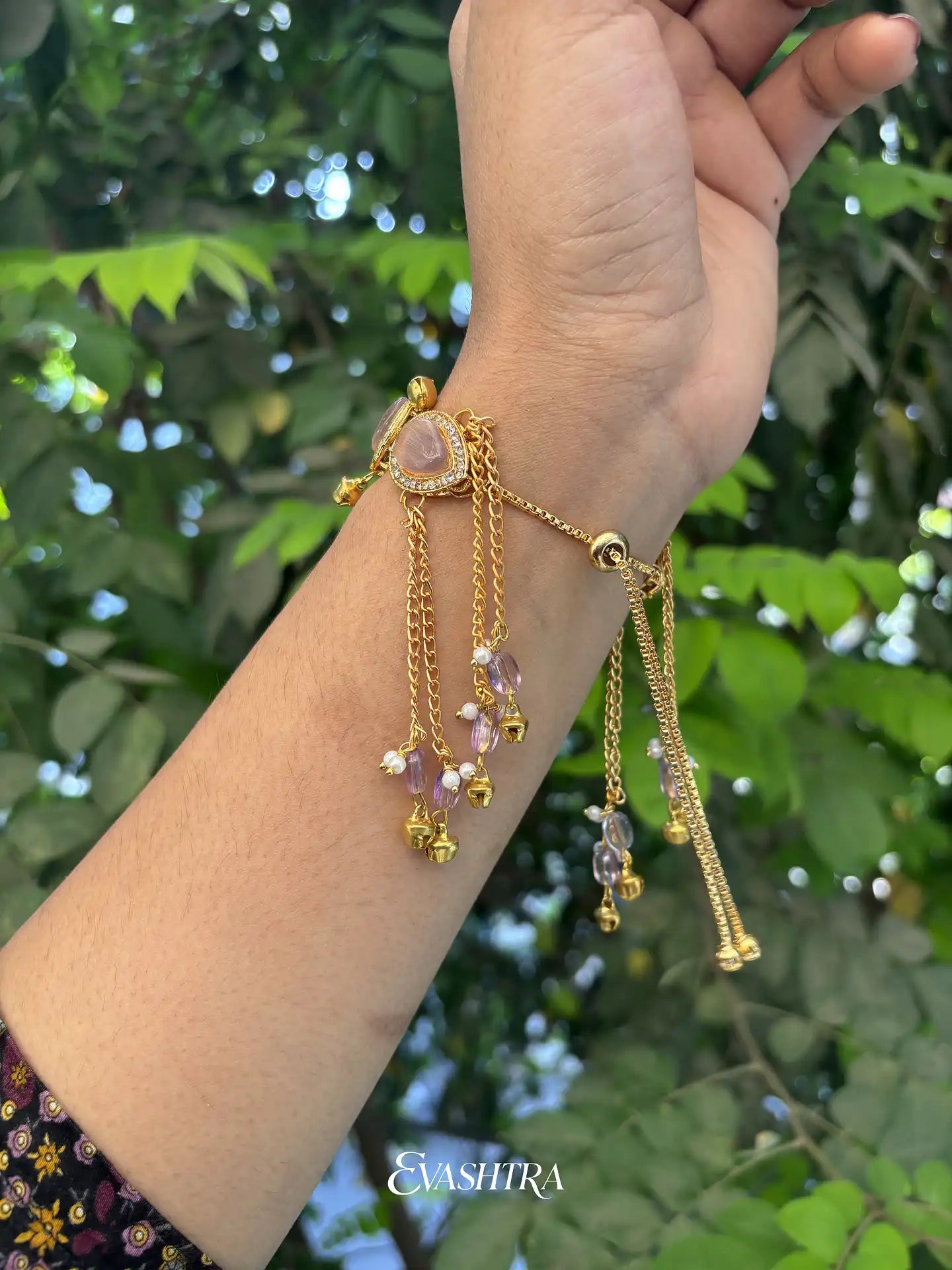 Gold bracelet with beads on a wrist against a green leafy background