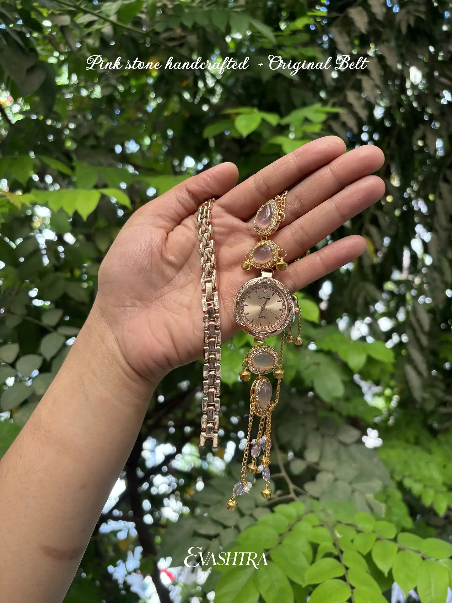 Hand holding a pink stone handcrafted belt with a blurred green leafy background