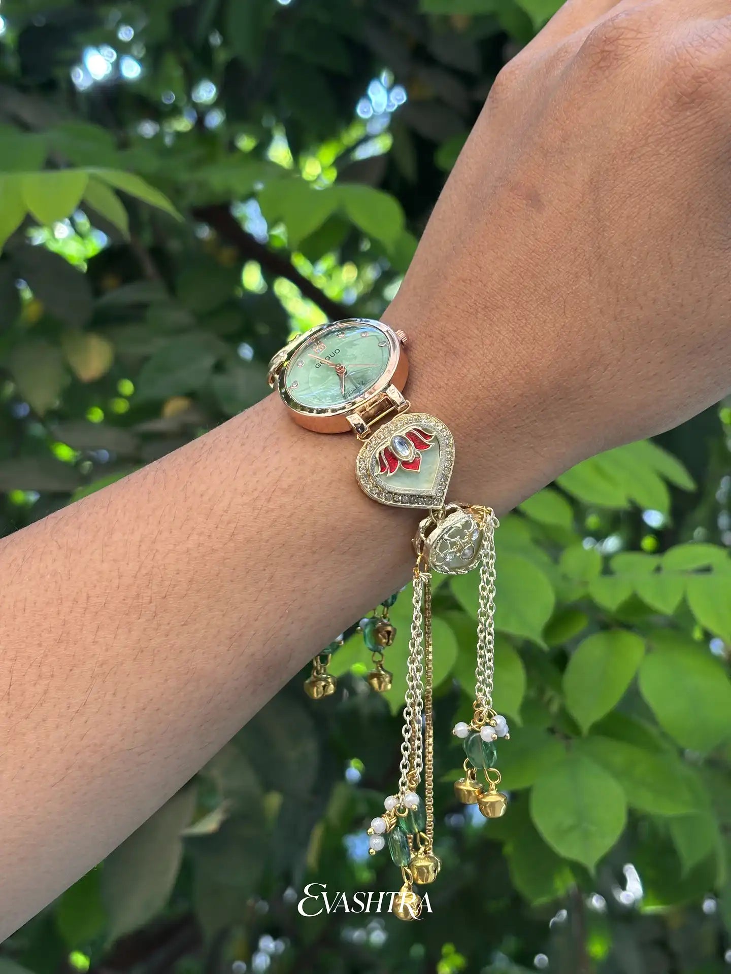 Gold watch with decorative chain on a wrist against a green leafy background