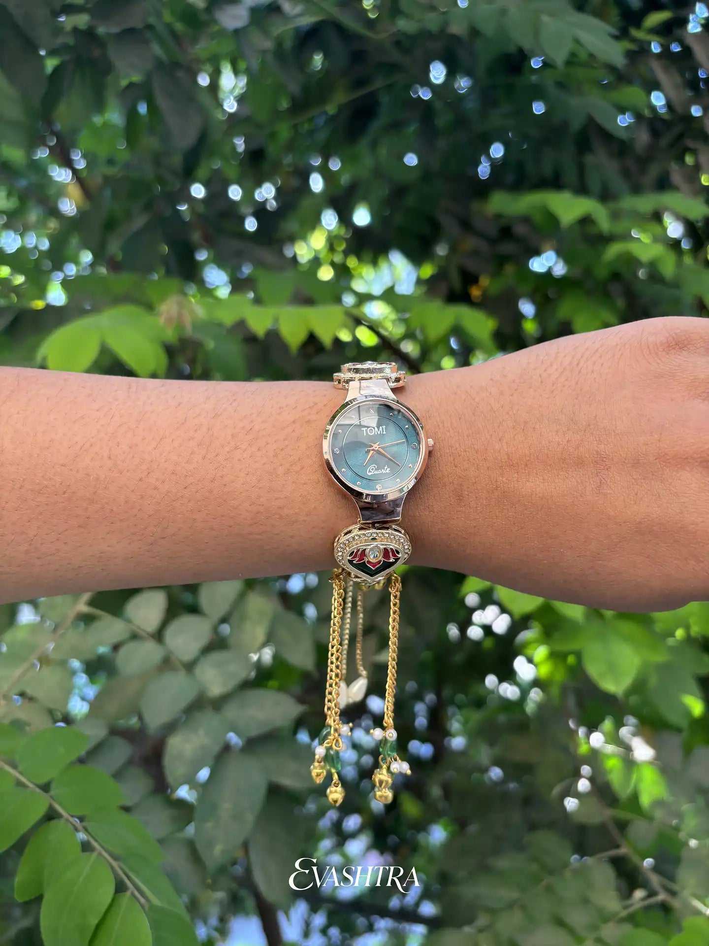 Gold watch with decorative chain on a wrist against a green leafy background