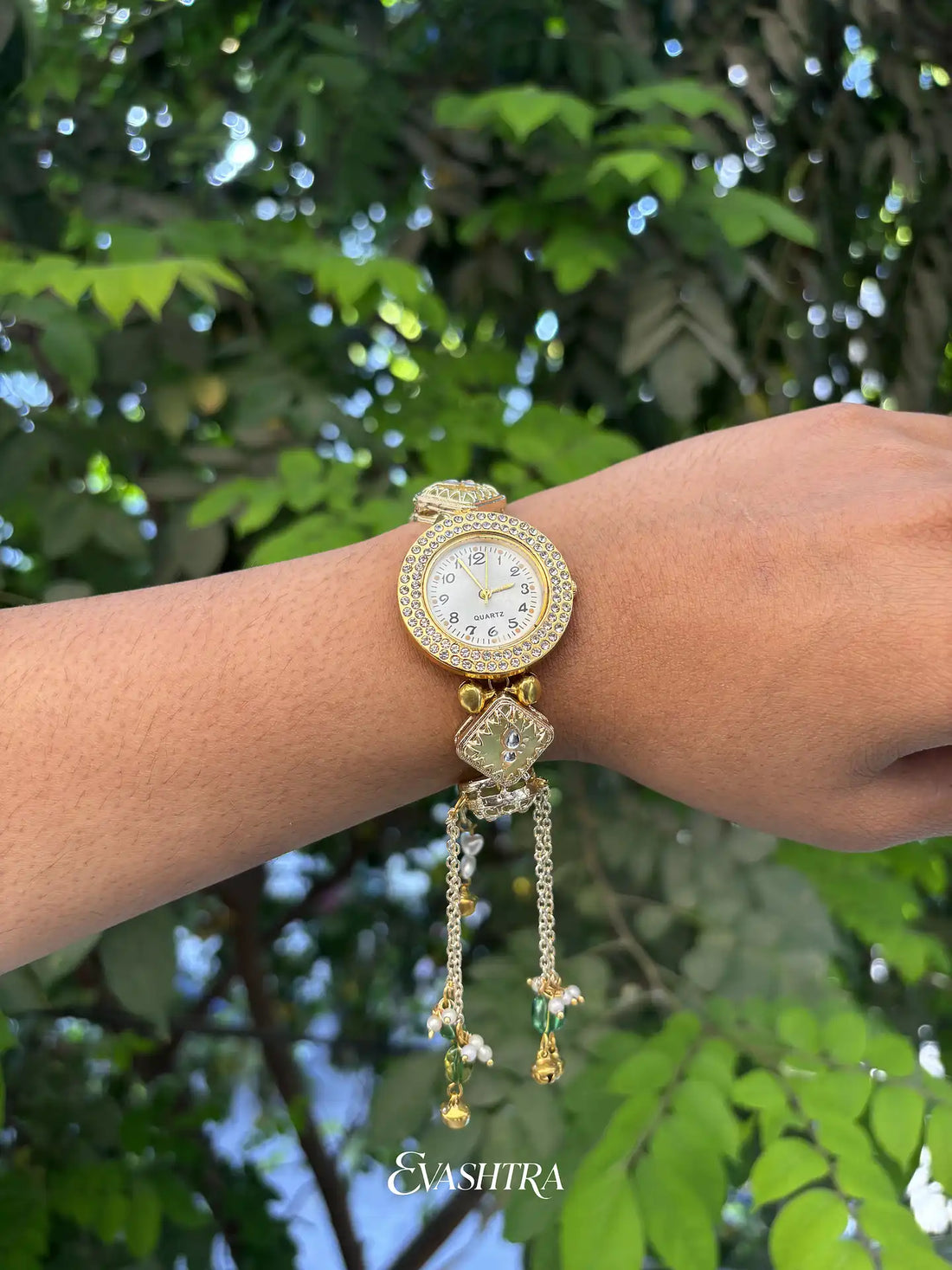 Gold wristwatch with decorative elements on a wrist against a green leafy background