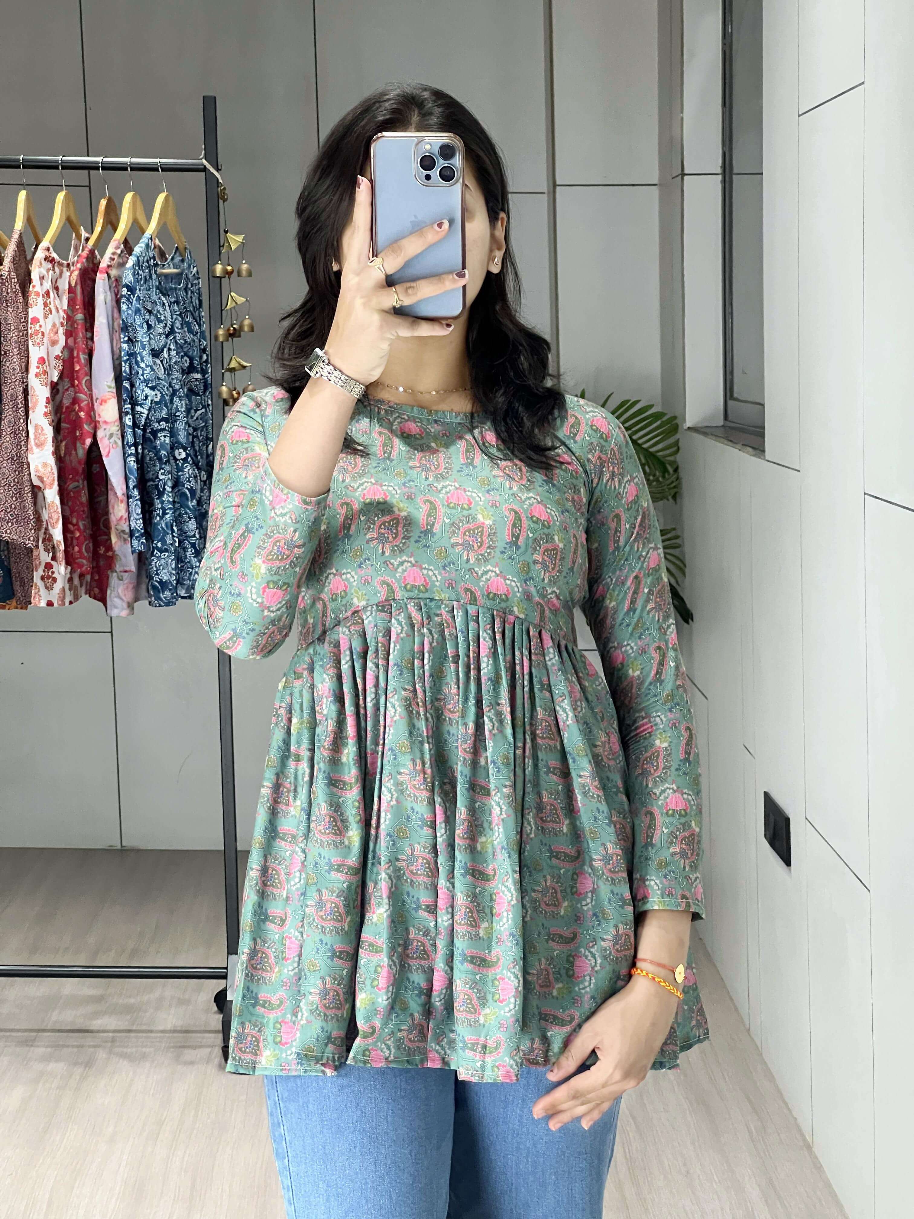 Person wearing a green floral dress in a room with clothing racks.