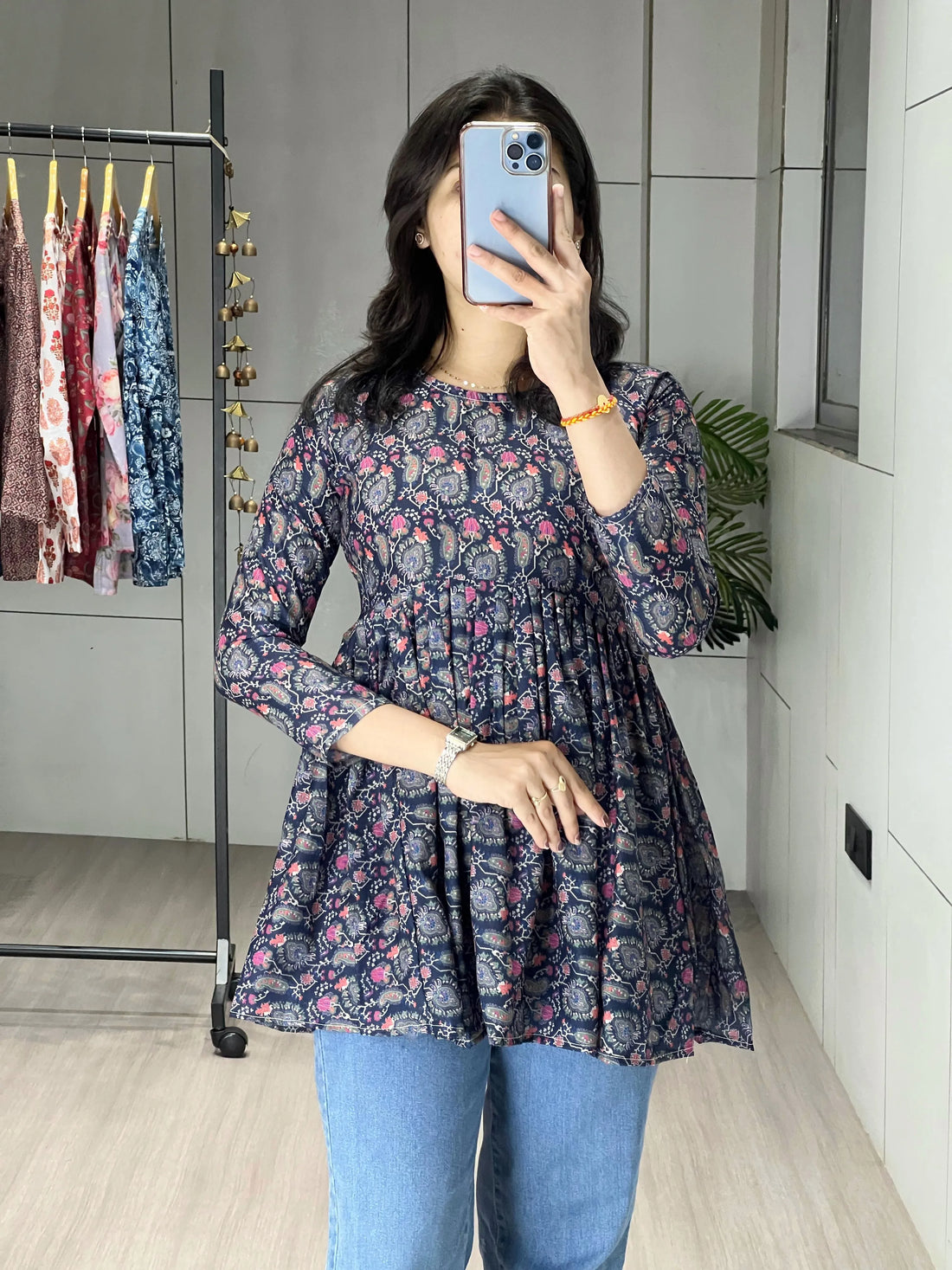 Person wearing a floral dress and blue jeans taking a mirror selfie.