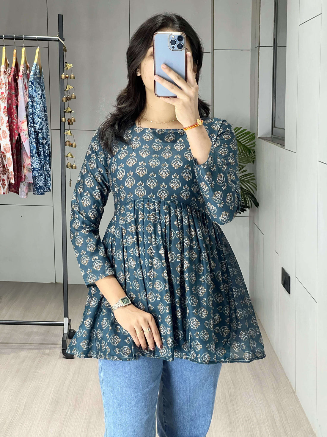 Person wearing a blue floral dress and blue jeans in a room with a clothing rack in the background.