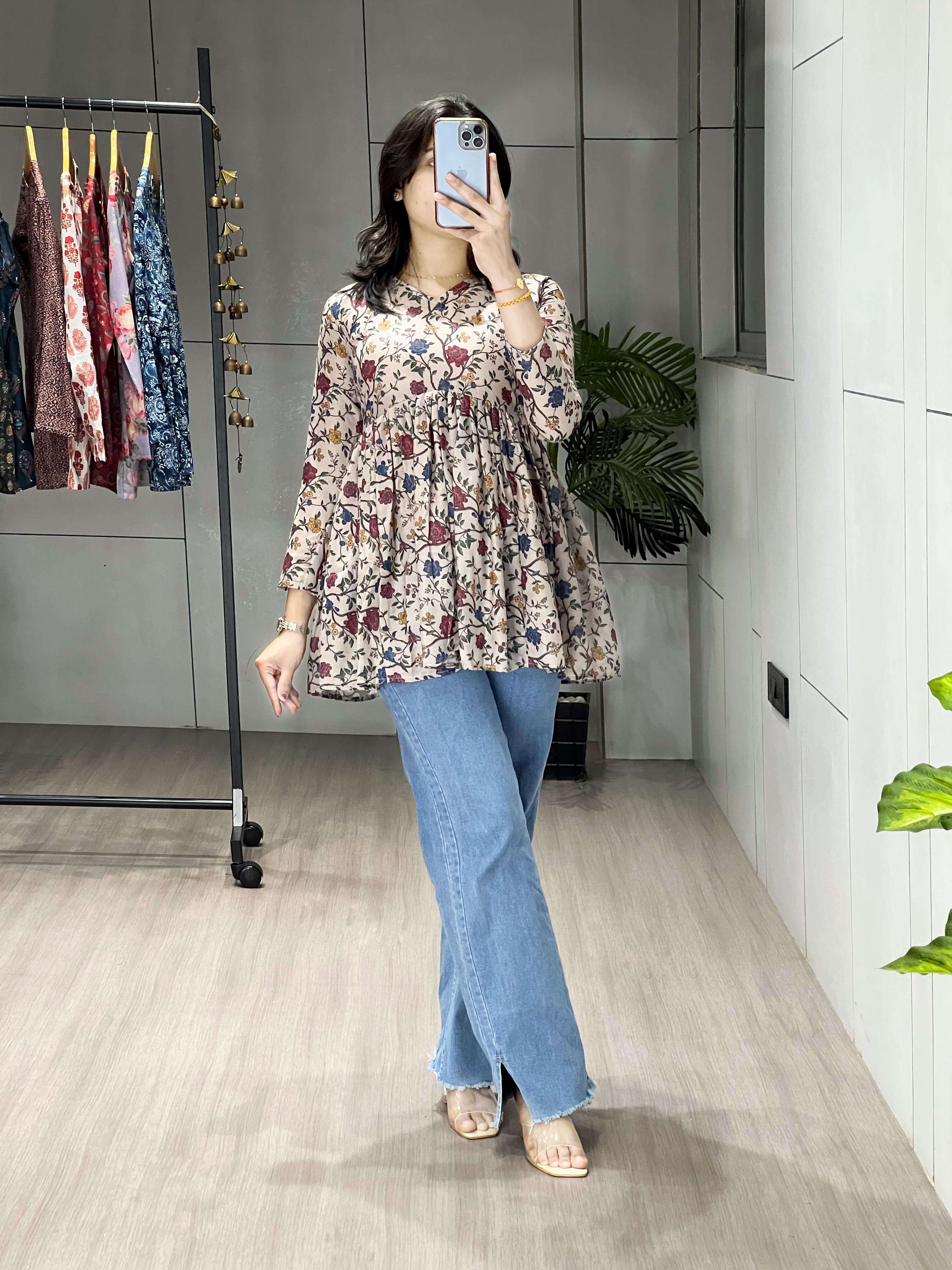 Woman taking a mirror selfie wearing a floral top and blue jeans in a clothing store.